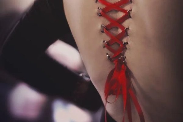 Gorsetowy piercing na plecach z czerwoną wstążką