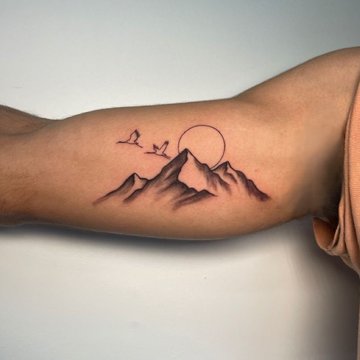 Tatuaż góry z ptakami na bicepsie mężczyzny