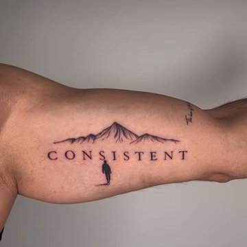 Tatuaż napis z górami na bicepsie mężczyzny