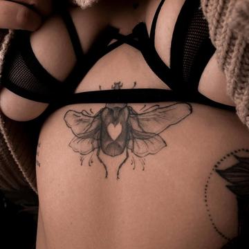 Czytelny tatuaż pod piersią: ćma z sercem