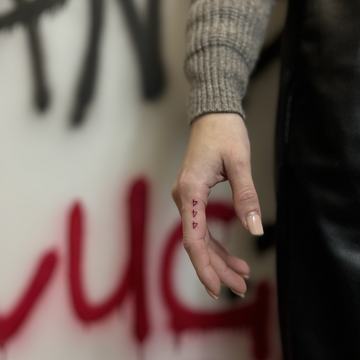 Tatuaż na palcu: trzy małe czerwone symbole