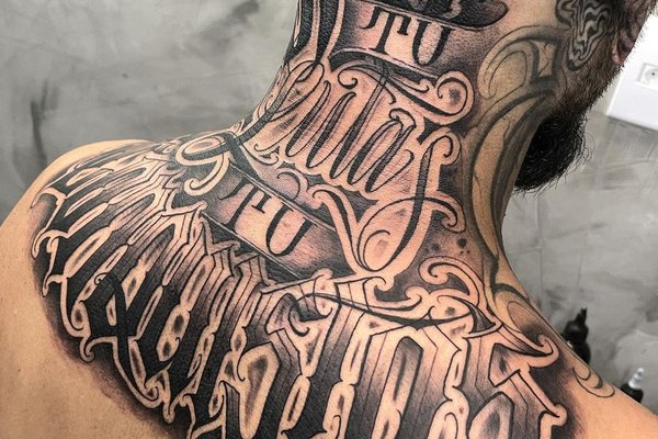 Tatuaż na karku i plecach z dużym napisem w ozdobnym stylu kaligraficznym