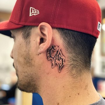 Tatuaż za uchem męski – czarno-szary napis w gotyckim stylu