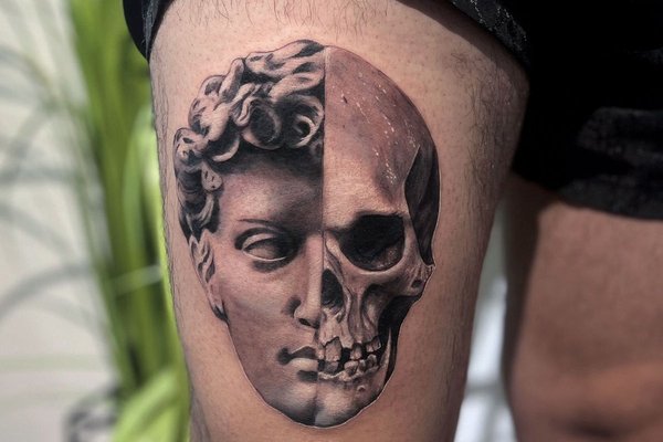 Tatuaż na udzie męski – połowa twarzy Davida i czaszka w realistycznym stylu