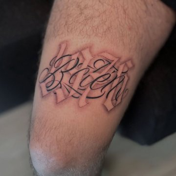 Tatuaż na udzie męski – napis w stylu kaligraficznym z cieniowaniem
