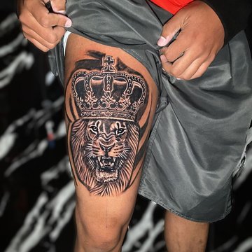 Tatuaż na udzie męski – realistyczny lew w koronie symbolizujący siłę i władzę
