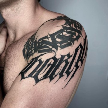 Tatuaż na barku męski – czarny gotycki napis w stylu blackwork
