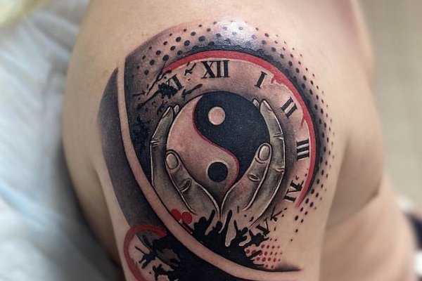 Tatuaż męski na barku - symbol yin i yang z zegarem w stylu trash polka