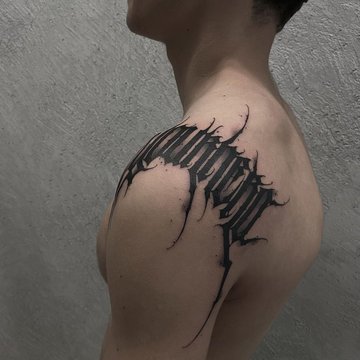 Tatuaż na barku męski - czarny napis z efektem rozerwanej skóry