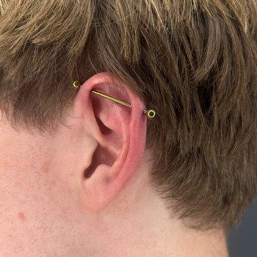 Złoty industrial piercing – pozioma sztanga w uchu