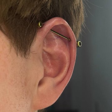 Złoty piercing industrial w chrząstce ucha