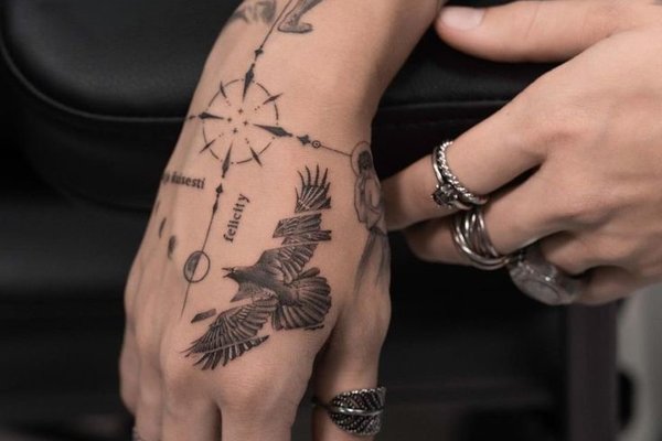 Delikatny tatuaż kompasu i ptaka na dłoni w stylu linework