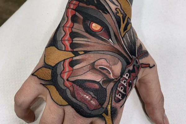 Kolorowy tatuaż motyla i twarzy na dłoni w stylu neotradycyjnym