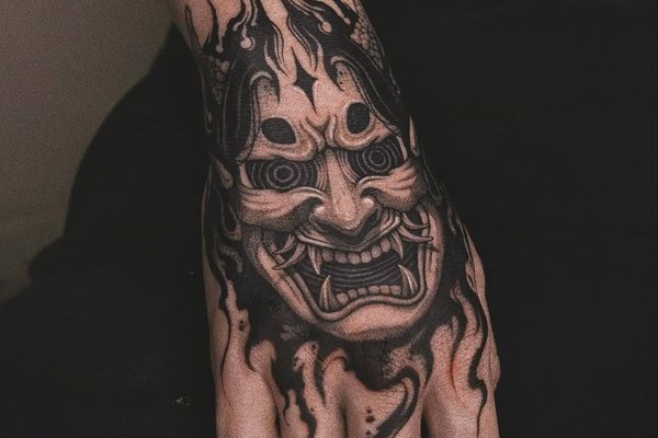 Tatuaż maski demona na dłoni w czarno-szarym stylu