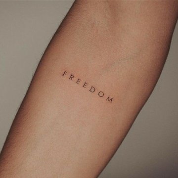 Minimalistyczny tatuaż z napisem Freedom na przedramieniu