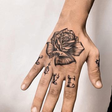 Tatuaż róża na dłoni litery na palcach – trudna strefa