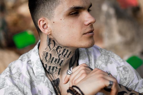 Czarne tatuaże na szyi i przedramieniu w słońcu